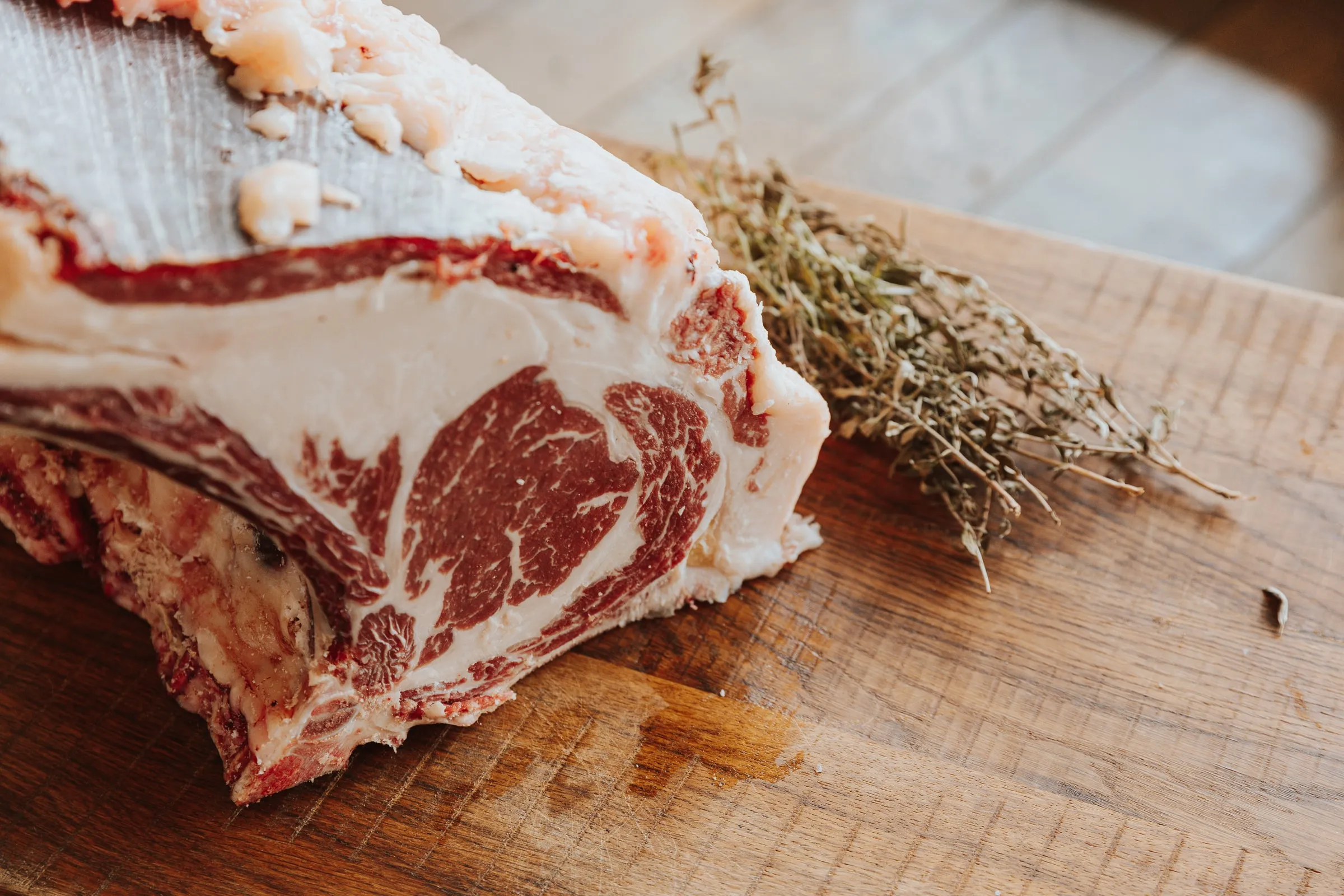 Een ribstuk met been van Angus Grand Cru op een houten plank, de rib-eye rijk gemarmerd, met tijm